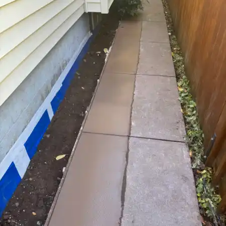 A completed exterior foundation waterproofing project with backfilled soil, sealed foundation walls, and freshly poured concrete walkways.