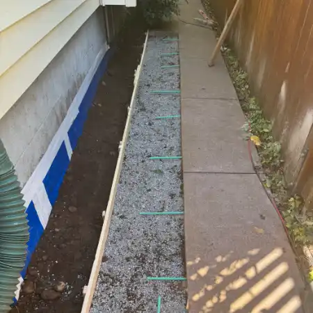 Exterior foundation preparation showing a gravel drainage bed and waterproofing barrier prior to final concrete pouring.
