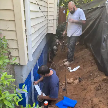 Masonry Masters technician's applying adhesive sealant to an exposed foundation wall in an excavated trench of residential home.