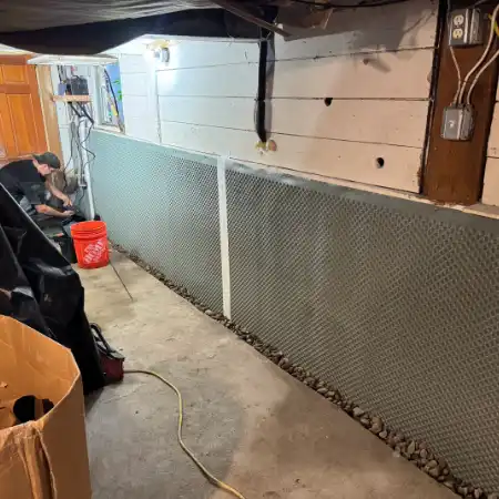 interior-basement-long-wall A technician installing an interior French drain and wall moisture barrier along a long basement wall.