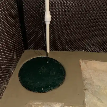 interior-basement-sump-pump A newly installed basement sump pump system with a green sealed basin cover, discharge pipe, and dimpled drainage membrane.